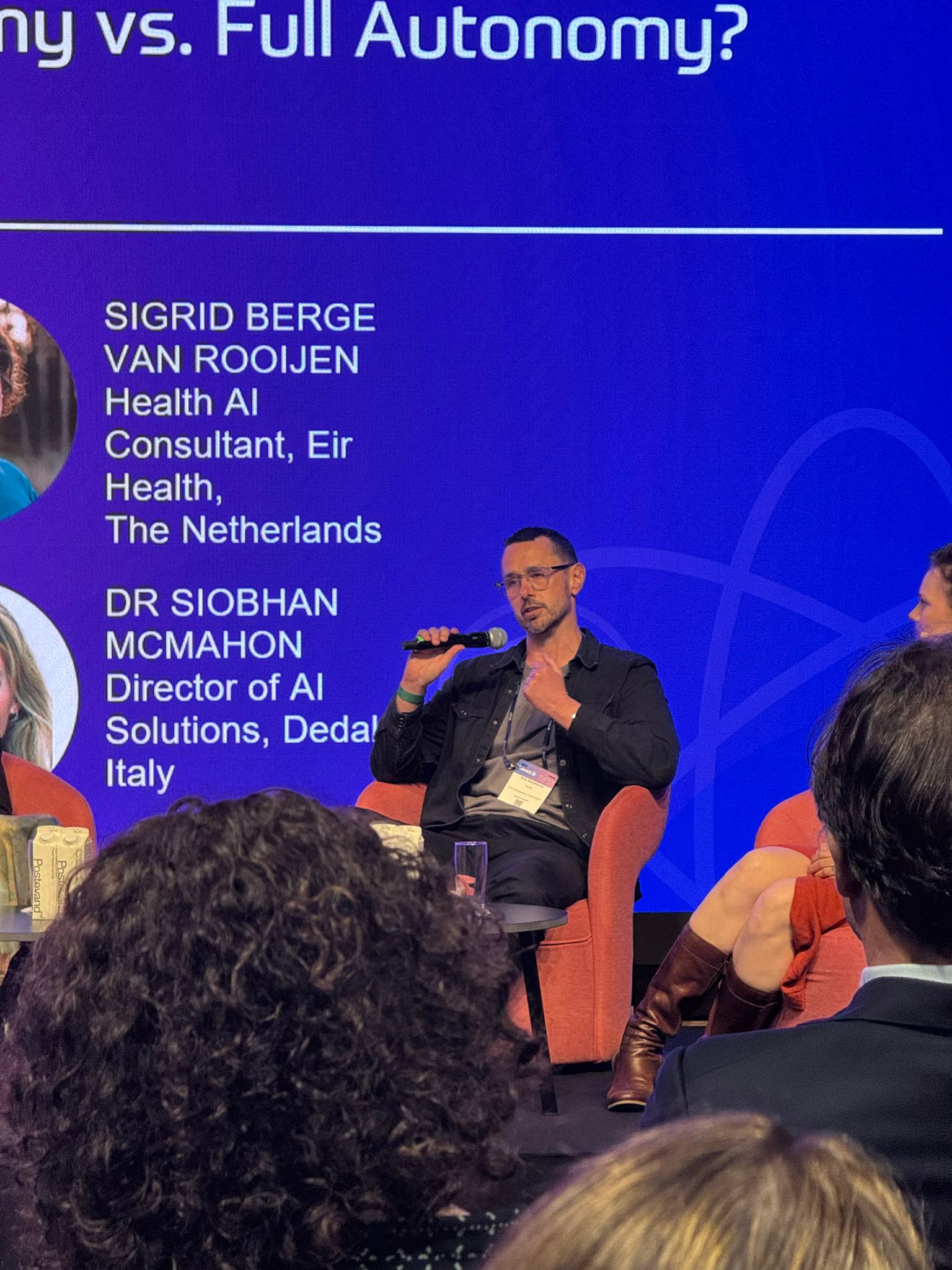 Russ Read-Barrow on stage at HIMSS Europe 2026, Copenhagen, speaking on a patient AI panel with a microphone in hand. Behind him a panel slide names co-panellists Sigrid Berge van Rooijen (Health AI Consultant, Eir Health, The Netherlands) and Dr Siobhan McMahon (Director of AI Solutions, Dedalus, Italy).